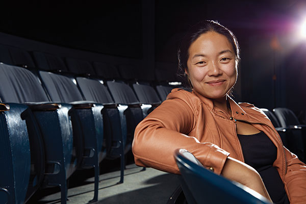 Desdemona Chiang sitting in a dark theatre with a light shining behind her.